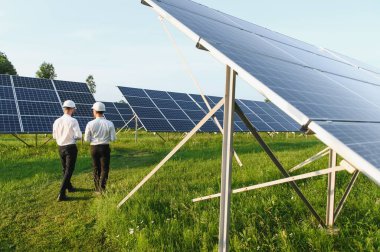 Güneş çiftliği (güneş paneli), iki mühendis ile birlikte sistemin işleyişini kontrol etmek için yürür, dünyanın enerjisini korumak için alternatif enerji, temiz enerji üretimi için fotovoltaik modül fikri