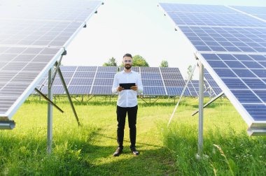 Fotovoltaik panellerin arka planında tableti olan erkek işçi güneş enerjisi santrali