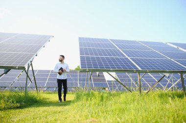 Fotovoltaik panellerin arka planında tableti olan erkek işçi güneş enerjisi santrali