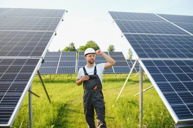 Erkek işçilerin güneş modülleri kurarken ve fotovoltaik güneş dizisini desteklerken yan görünümü. Güneş paneliyle çalışırken kaskını takan bir elektrikçi. Güneş enerjisi kavramı.
