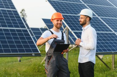 Güneş enerjisi bataryalarının yakınında bir işadamı ve işçi. İş müşterisi ustabaşına fotovoltaik detayları gösteriyor. İki adam anlaşma yapıyor.