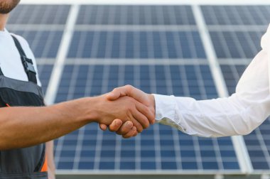 Workers shaking hands on a background of solar panels on solar power plant