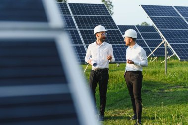 Güneş çiftliği (güneş paneli), iki mühendis ile birlikte sistemin işleyişini kontrol etmek için yürür, dünyanın enerjisini korumak için alternatif enerji, temiz enerji üretimi için fotovoltaik modül fikri.