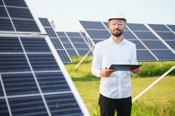 Positive bearded male investor standing against photovoltaic panels producing alternative energy