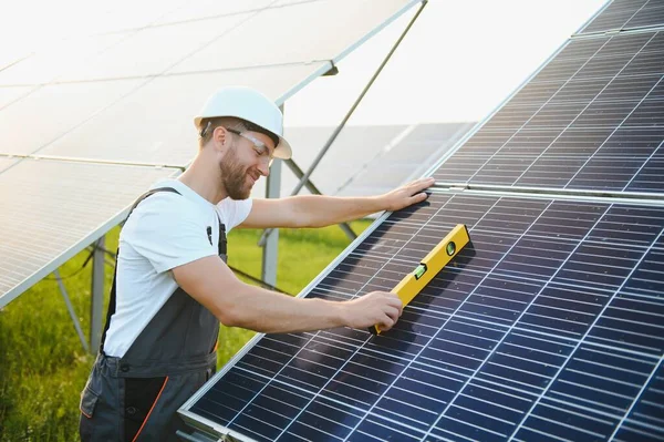 Erkek işçilerin güneş modülleri kurarken ve fotovoltaik güneş dizisini desteklerken yan görünümü. Güneş paneliyle çalışırken kaskını takan bir elektrikçi. Güneş enerjisi kavramı.