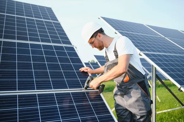 ドリルと一様の男性労働者 太陽電池パネルの近くのステッダーに彼の手のドライバー — ストック写真