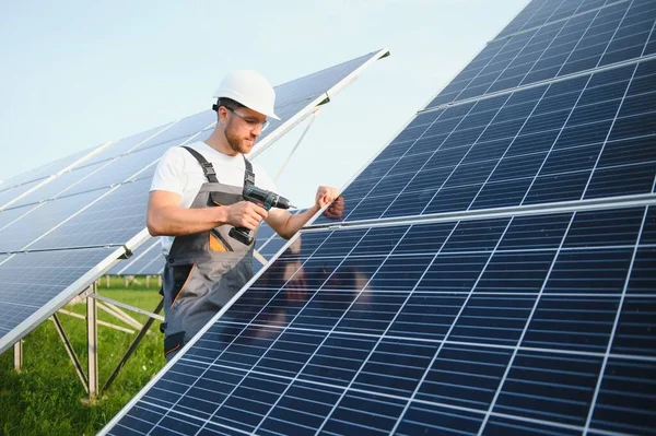 ドリルと一様の男性労働者 太陽電池パネルの近くのステッダーに彼の手のドライバー — ストック写真