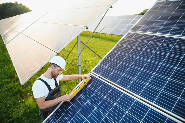 太陽電池モジュールを設置し 太陽電池アレイの構造をサポートする男性労働者の側面図 ソーラーパネルで作業中に安全ヘルメットをかぶっている電気技師 太陽エネルギーの概念 — ストック写真