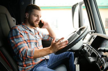Genç profesyonel sürücü kamyon kullanırken cep telefonuyla iletişim kuruyor.