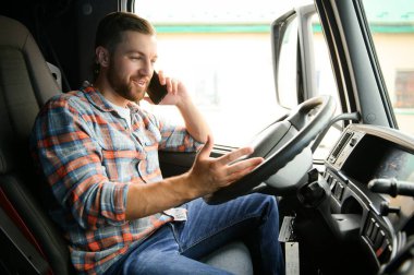 Genç profesyonel sürücü kamyon kullanırken cep telefonuyla iletişim kuruyor.
