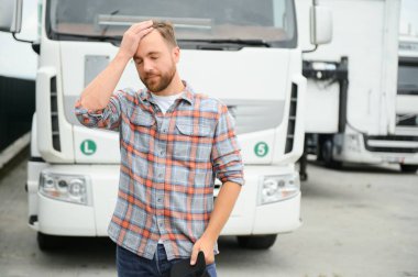 Yoldan yorgun düşen kamyon şoförü beyaz kamyonetinin yanında duruyor.
