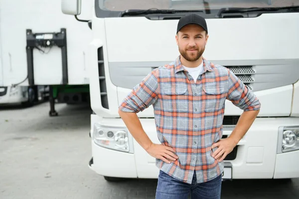 Portrait of young Caucasian bearded trucker standing by his truck vehicle. Transportation service. Truck driver job