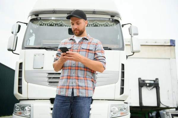 Professional driver using mobile phone while standing in front of his truck. Copy space