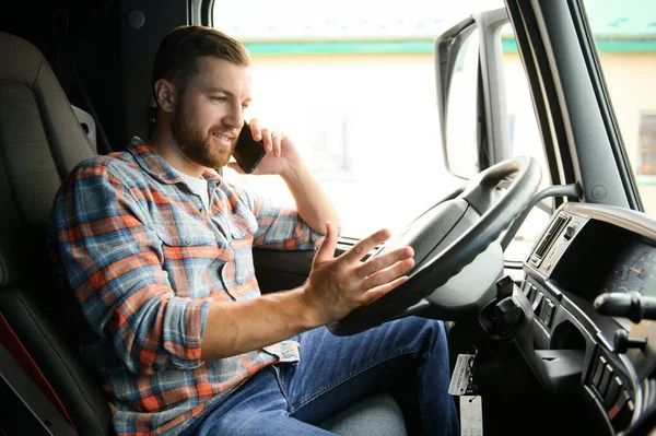 Genç profesyonel sürücü kamyon kullanırken cep telefonuyla iletişim kuruyor.