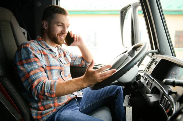 Genç profesyonel sürücü kamyon kullanırken cep telefonuyla iletişim kuruyor.