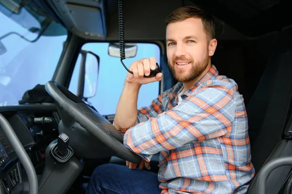 Man trucker driving in a cabin of his truck and talking on radio transmitter