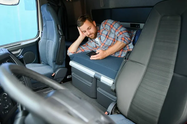 A trucker in the cab, lying in the truck bed, scrolling on his phone during his spare time