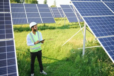 Genç Hintli erkek mühendisin portresi güneş panellerinin yanında duruyor, açık mavi gökyüzü arka planı, yenilenebilir ve temiz enerjisi var. beceri Hindistan, kopyalama alanı