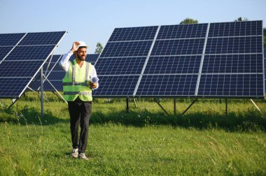 Yeşil yelekli Hintli bir erkek mühendis güneş panelleri üzerinde çalışıyor. Yenilenebilir enerji kavramı