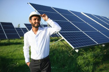 Genç Hintli erkek mühendisin portresi güneş panellerinin yanında duruyor, açık mavi gökyüzü arka planı, yenilenebilir ve temiz enerjisi var. beceri Hindistan, kopyalama alanı