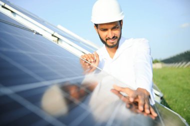 Genç Hintli erkek mühendisin portresi güneş panellerinin yanında duruyor, açık mavi gökyüzü arka planı, yenilenebilir ve temiz enerjisi var. beceri Hindistan, kopyalama alanı