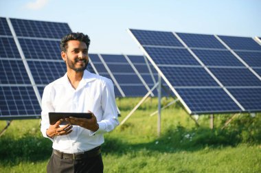 Genç Hintli teknisyen ya da yönetici güneş panelinin yanında duran resmi giysiler giyiyor. Yenilenebilir enerji, çapraz duran adam, boşluğu kopyala.