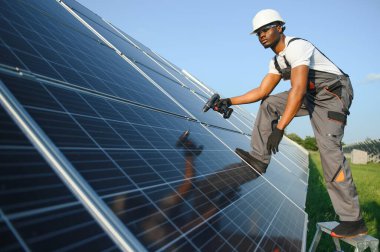 Güvenlik kaskı ve üniforma takan Afro-Amerikan elektrik mühendisinin portresi güneş panelleri kuruyor.