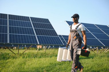 Güvenlik kaskı ve üniforma takan Afro-Amerikan elektrik mühendisinin portresi güneş panelleri kuruyor.