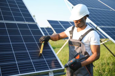 Güneş pili panellerini koruyan Afrikalı Amerikalı mühendis. Ekolojik güneş çiftliği inşaatında çalışan bir teknisyen. Yenilenebilir temiz enerji teknolojisi kavramı.