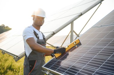 Güneş pili panellerini koruyan Afrikalı Amerikalı mühendis. Ekolojik güneş çiftliği inşaatında çalışan bir teknisyen. Yenilenebilir temiz enerji teknolojisi kavramı.