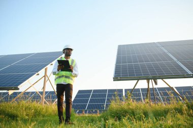 Afrikalı Amerikalı teknisyen güneş panellerinin bakımını kontrol ediyor. Güneş istasyonundaki siyah adam mühendisi.