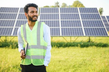 Genç Hintli erkek mühendisin portresi güneş panellerinin yanında duruyor, açık mavi gökyüzü arka planı, yenilenebilir ve temiz enerjisi var. beceri Hindistan, kopyalama alanı
