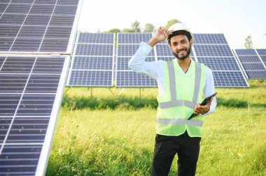 Genç Hintli erkek mühendisin portresi güneş panellerinin yanında duruyor, açık mavi gökyüzü arka planı, yenilenebilir ve temiz enerjisi var. beceri Hindistan, kopyalama alanı