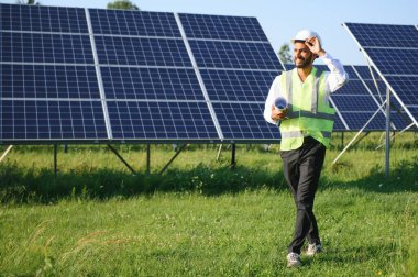 Genç Hintli erkek mühendisin portresi güneş panellerinin yanında duruyor, açık mavi gökyüzü arka planı, yenilenebilir ve temiz enerjisi var. beceri Hindistan, kopyalama alanı