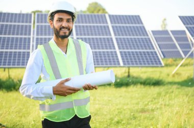 Genç Hintli erkek mühendisin portresi güneş panellerinin yanında duruyor, açık mavi gökyüzü arka planı, yenilenebilir ve temiz enerjisi var. beceri Hindistan, kopyalama alanı