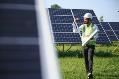 Genç Hintli erkek mühendisin portresi güneş panellerinin yanında duruyor, açık mavi gökyüzü arka planı, yenilenebilir ve temiz enerjisi var. beceri Hindistan, kopyalama alanı