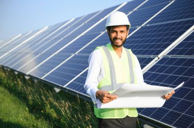 Genç Hintli erkek mühendisin portresi güneş panellerinin yanında duruyor, açık mavi gökyüzü arka planı, yenilenebilir ve temiz enerjisi var. beceri Hindistan, kopyalama alanı