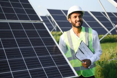 Genç Hintli erkek mühendisin portresi güneş panellerinin yanında duruyor, açık mavi gökyüzü arka planı, yenilenebilir ve temiz enerjisi var. beceri Hindistan, kopyalama alanı