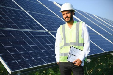 Genç Hintli erkek mühendisin portresi güneş panellerinin yanında duruyor, açık mavi gökyüzü arka planı, yenilenebilir ve temiz enerjisi var. beceri Hindistan, kopyalama alanı