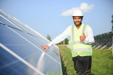 Genç Hintli teknisyen ya da yönetici güneş panelinin yanında duran resmi giysiler giyiyor. Yenilenebilir enerji, çapraz duran adam, boşluğu kopyala.