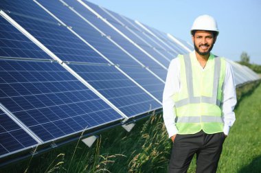 Genç Hintli erkek mühendisin portresi güneş panellerinin yanında duruyor, açık mavi gökyüzü arka planı, yenilenebilir ve temiz enerjisi var. beceri Hindistan, kopyalama alanı