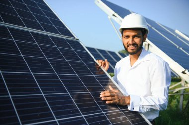Genç Hintli erkek mühendisin portresi güneş panellerinin yanında duruyor, açık mavi gökyüzü arka planı, yenilenebilir ve temiz enerjisi var. beceri Hindistan, kopyalama alanı