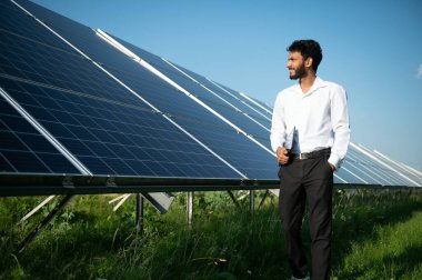 Genç Hintli erkek mühendisin portresi güneş panellerinin yanında duruyor, açık mavi gökyüzü arka planı, yenilenebilir ve temiz enerjisi var. beceri Hindistan, kopyalama alanı
