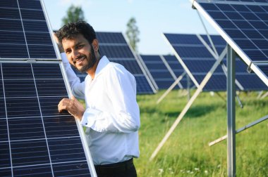 Genç Hintli erkek mühendisin portresi güneş panellerinin yanında duruyor, açık mavi gökyüzü arka planı, yenilenebilir ve temiz enerjisi var. beceri Hindistan, kopyalama alanı