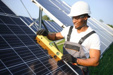 Güneş pili panellerini koruyan Afrikalı Amerikalı mühendis. Ekolojik güneş çiftliği inşaatında çalışan bir teknisyen. Yenilenebilir temiz enerji teknolojisi kavramı.