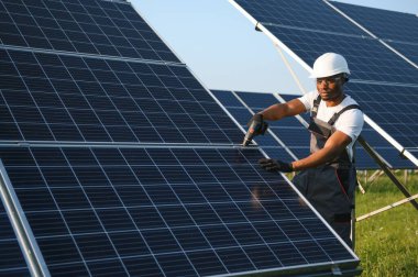 Güvenlik kaskı ve üniforma takan Afro-Amerikan elektrik mühendisinin portresi güneş panelleri kuruyor.