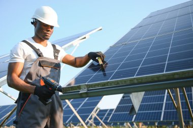 Güvenlik kaskı ve üniforma takan Afro-Amerikan elektrik mühendisinin portresi güneş panelleri kuruyor.