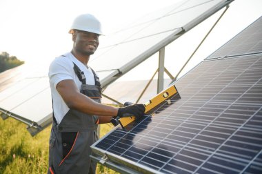 Güvenlik kaskı ve üniforma takan Afro-Amerikan elektrik mühendisinin portresi güneş panelleri kuruyor.