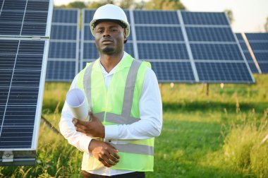 Genç, yakışıklı Afrikalı Amerikalı zanaatkârın yakın portresi koruyucu bir miğfer. Tulumlu, kameraya gülümseyen mutlu bir adam. Yavaş çekim