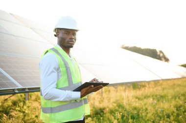 Afrikalı Amerikalı teknisyen güneş panellerinin bakımını kontrol ediyor. Güneş istasyonundaki siyah adam mühendisi.